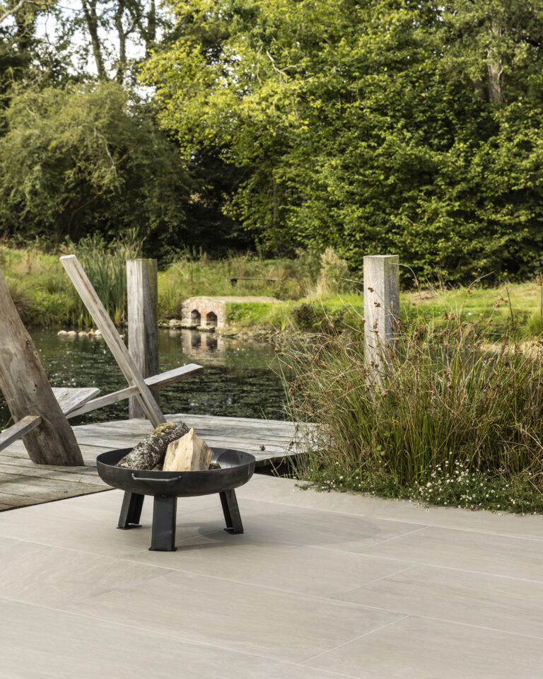 Lakeside patio with log burner and small wooden dock tiled with Chiltern Buff Outdoor porcelain tiles
