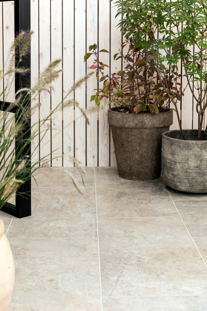 Patio area with plant pots against contemporary wooden fence. Paved with Mandarin Stone Hendre Blanc Porcelain outdoor tiles