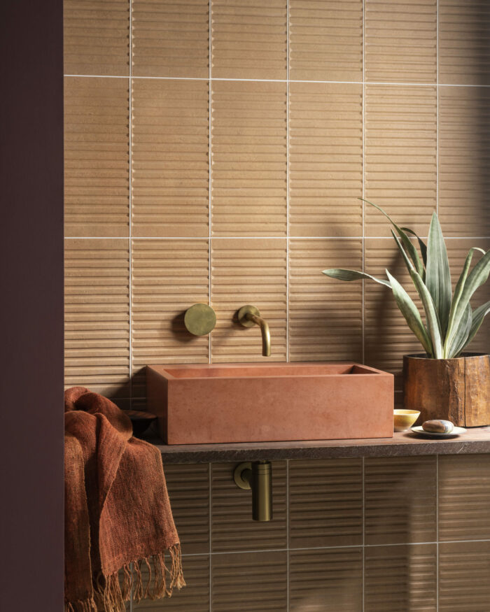 Bar Terra Ceramic textured wall tiles in bathroom with contemporary square countertop sink, gold fixtures and orange decor