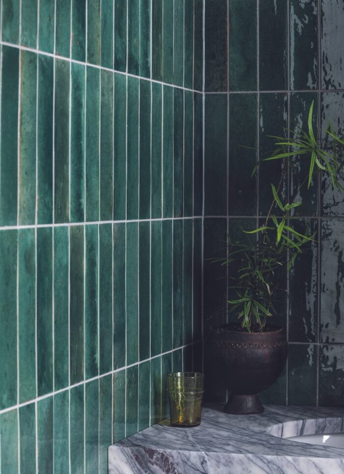 Dark green Zellige tiles on the wall behind a marble sink basin.