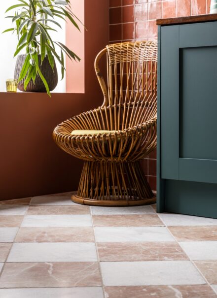 Rosso Di Scacchi Tumbled Marble tiles lay on the floor with a wicker chair sat in front of the Zellige Coral Gloss Ceramic tiles on the wall.