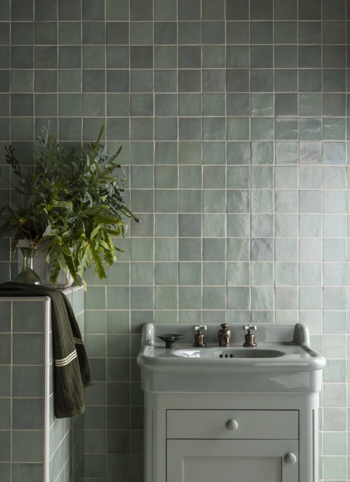 Mint green zellige style tiles on a bathroom wall behind a matching green sink.